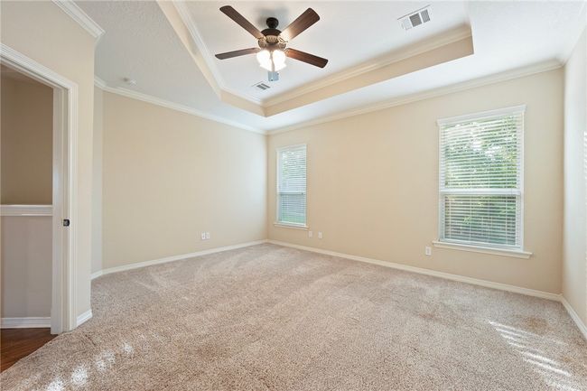 Carpeted empty room with a raised ceiling, ornamental molding, and a ceiling fan | Image 11