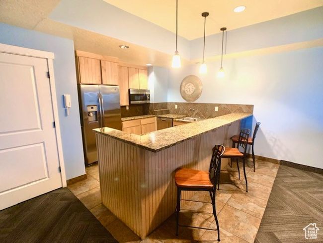 Kitchen with appliances with stainless steel finishes, a peninsula, a kitchen bar, light brown cabinetry, and stone countertops | Image 6