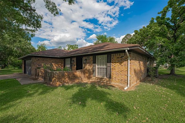 This charming single-story brick home features a classic design with a low-pitched roof and large front windows. It is surrounded by lush greenery and mature trees, offering a serene and private setting. The property includes a small front patio and a spacious lawn, ideal for outdoor activities. | Image 32