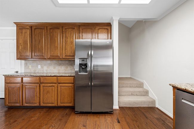 Kitchen featuring brown cabinetry, stainless steel appliances, backsplash, light stone countertops, and dark wood-style floors | Image 12