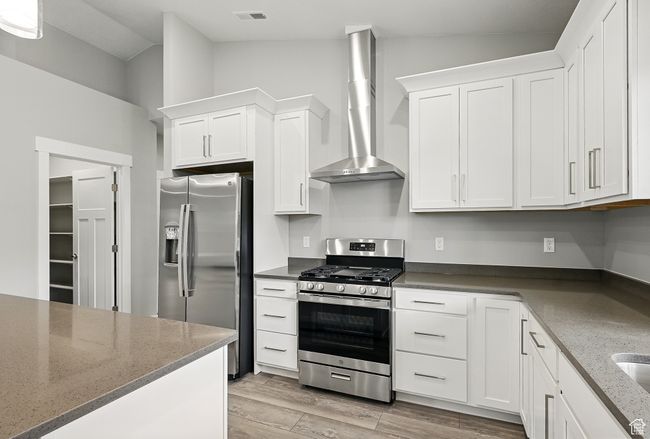 Kitchen with appliances with stainless steel finishes, wall chimney range hood, white cabinetry, vaulted ceiling, and light wood-type flooring | Image 19