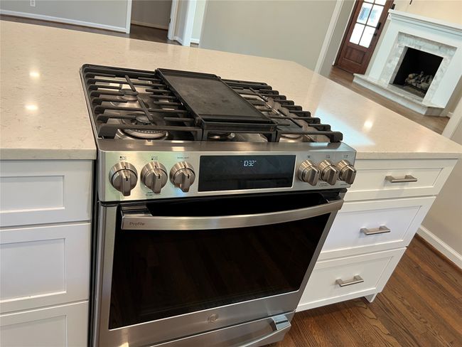 Kitchen view of dark wood-type flooring, light stone counters, stainless steel gas range, and white cabinets | Image 14