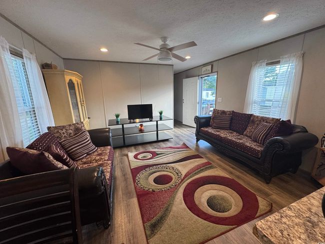 Living area featuring wood finished floors, ornamental molding, a textured ceiling, a ceiling fan, and a decorative wall | Image 4