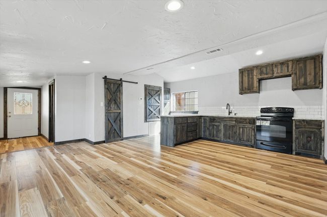 Kitchen with light wood finished floors, black range with electric stovetop, a barn door, a peninsula, and a sink | Image 6
