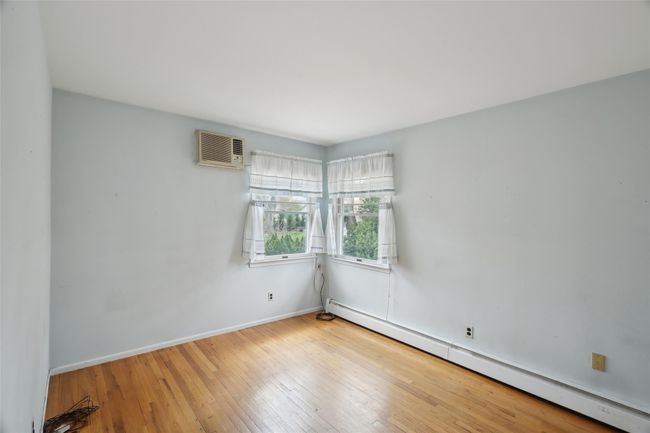 Unfurnished room featuring a baseboard heating unit, a wall mounted air conditioner, wood-type flooring, and baseboards | Image 22