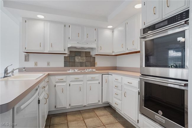 Kitchen featuring white cabinets, under cabinet range hood, white appliances, and a sink | Image 16
