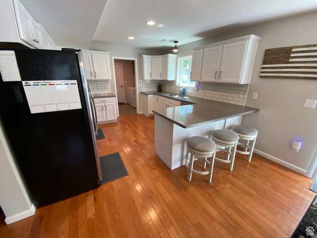 Kitchen with freestanding refrigerator, a peninsula, a kitchen bar, light wood finished floors, and a sink | Image 7