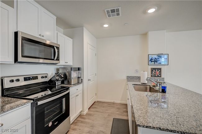 Kitchen with appliances with stainless steel finishes, a peninsula, light wood-type flooring, white cabinets, and light stone counters | Image 13