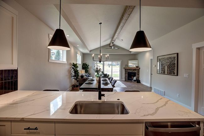 Kitchen featuring light stone counters, an island with sink, a stone fireplace, and open floor plan | Image 11