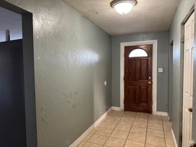 Doorway to outside featuring a textured ceiling, light tile patterned flooring, baseboards, and a textured wall | Image 10