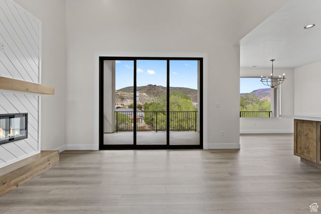 Unfurnished living room with light wood finished floors, baseboards, a notable chandelier, and a glass covered fireplace | Image 4