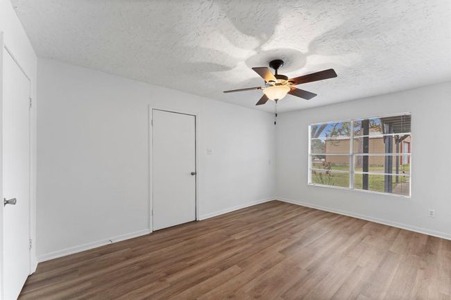 This room features a ceiling fan and a large window offering ample natural light. It has wood-look flooring and neutral walls, providing a clean and modern look. | Image 29
