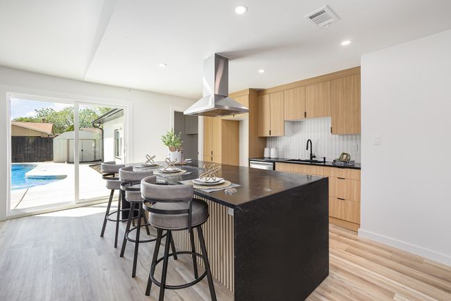 Kitchen with tasteful backsplash, dark countertops, visible vents, island range hood, and light brown cabinetry | Image 17