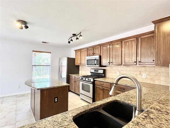 Kitchen featuring appliances with stainless steel finishes, light stone counters, decorative backsplash, a kitchen island, and a textured ceiling | Image 19