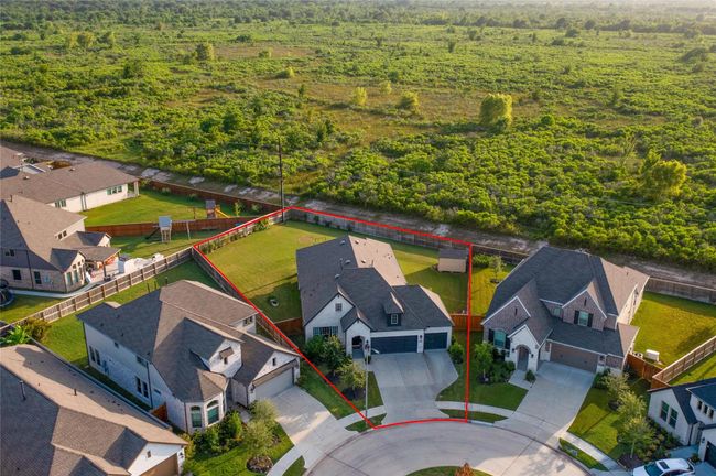 This photo shows a charming home at the end of a cul-de-sac, featuring a spacious backyard with a red outline and scenic views of lush greenery beyond the fence. The neighborhood appears peaceful and well-maintained. | Image 7