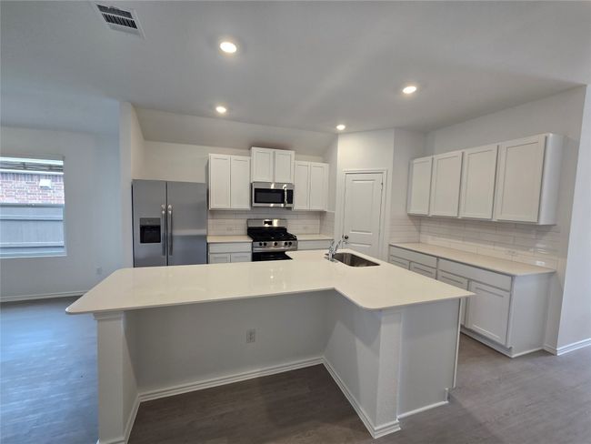 Kitchen with stainless steel appliances, backsplash, a center island with sink, light countertops, and dark wood-style flooring | Image 8