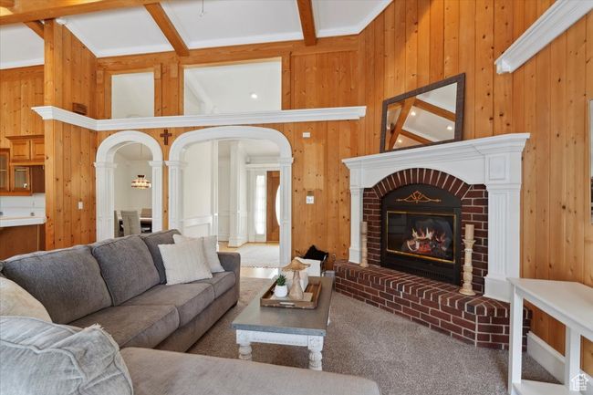 Carpeted living room with wooden walls, a fireplace, arched walkways, beam ceiling, and decorative columns | Image 5