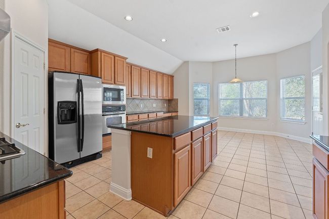Kitchen featuring light tile patterned flooring, visible vents, stainless steel appliances, a center island, and backsplash | Image 9
