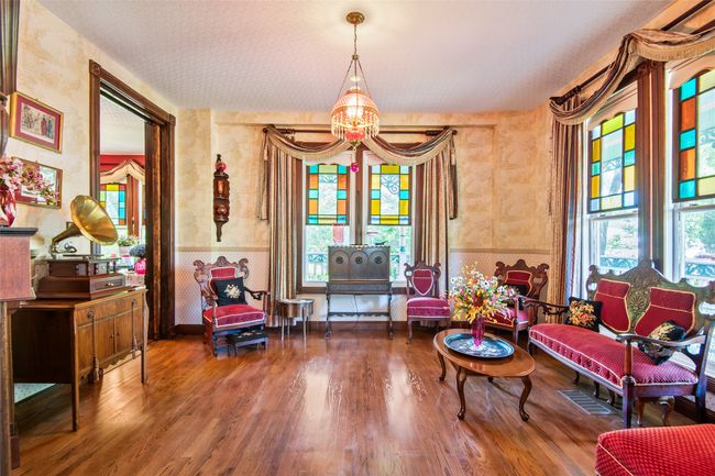 Sitting room with wallpapered walls, a chandelier, wood finished floors, wainscoting, and pocket doors | Image 6