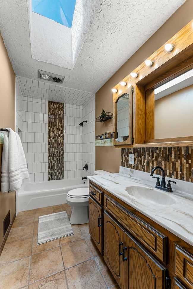 The full bathroom is thoughtfully designed with a skylight for enhanced natural light, a combined tub and shower with a tile surround, tile flooring, a single vanity with ample counter space, and a heat lamp for additional warmth and comfort. | Image 12