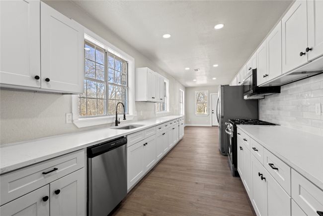 Kitchen featuring stainless steel appliances, light countertops, backsplash, white cabinetry, and a sink | Image 6