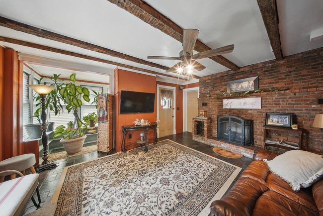 Living room featuring plenty of natural light, stone tile flooring, ceiling fan, a brick fireplace, and beamed ceiling | Image 4