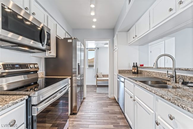 Kitchen with stainless steel appliances, a sink, wood finished floors, white cabinetry, and light stone counters | Image 14