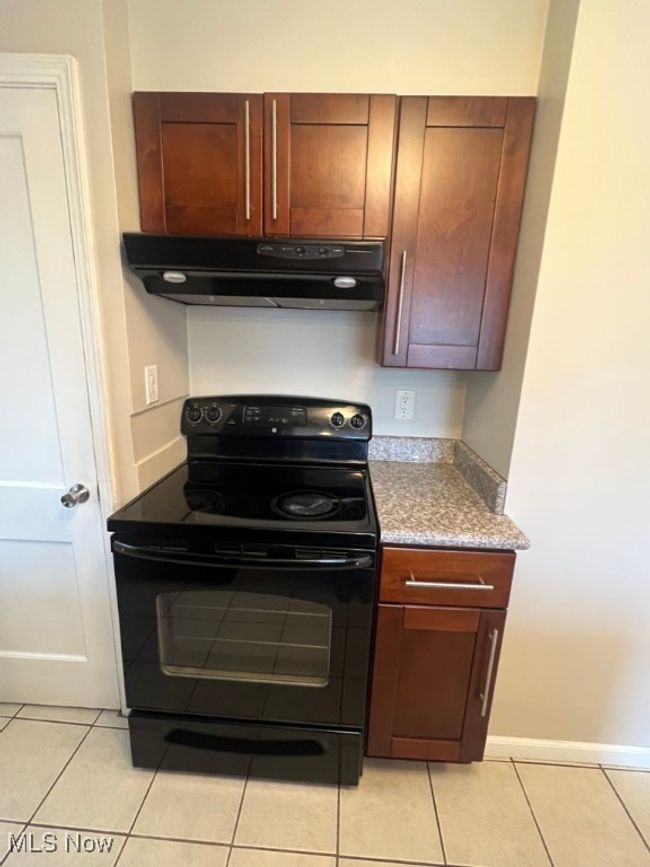 Kitchen featuring black electric range oven, exhaust hood, light tile floors, and granite countertops | Image 23