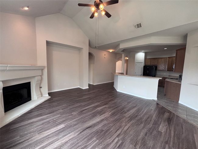 Unfurnished living room featuring arched walkways, a ceiling fan, lofted ceiling, dark wood finished floors, and a premium fireplace | Image 14