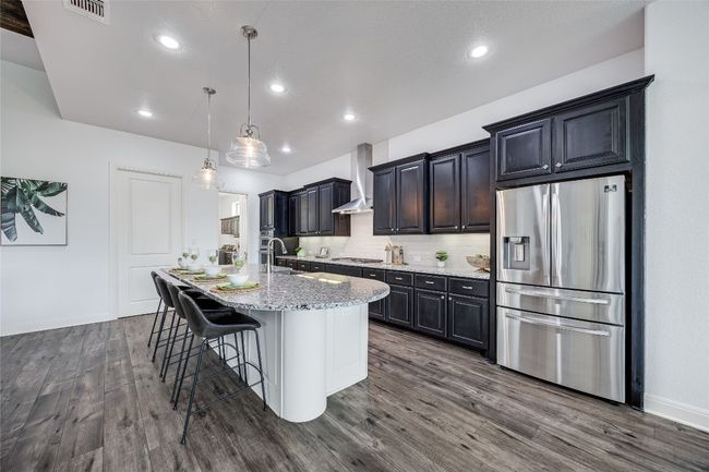 Kitchen featuring appliances with stainless steel finishes, wall chimney exhaust hood, dark wood-style flooring, a center island with sink, and a breakfast bar area | Image 9