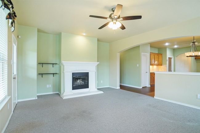 Unfurnished living room featuring baseboards, arched walkways, dark colored carpet, and a ceiling fan | Image 14