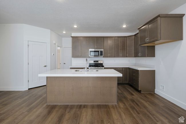 Kitchen with dark wood-style floors, a kitchen island with sink, stainless steel appliances, light countertops, and dark brown cabinets | Image 7