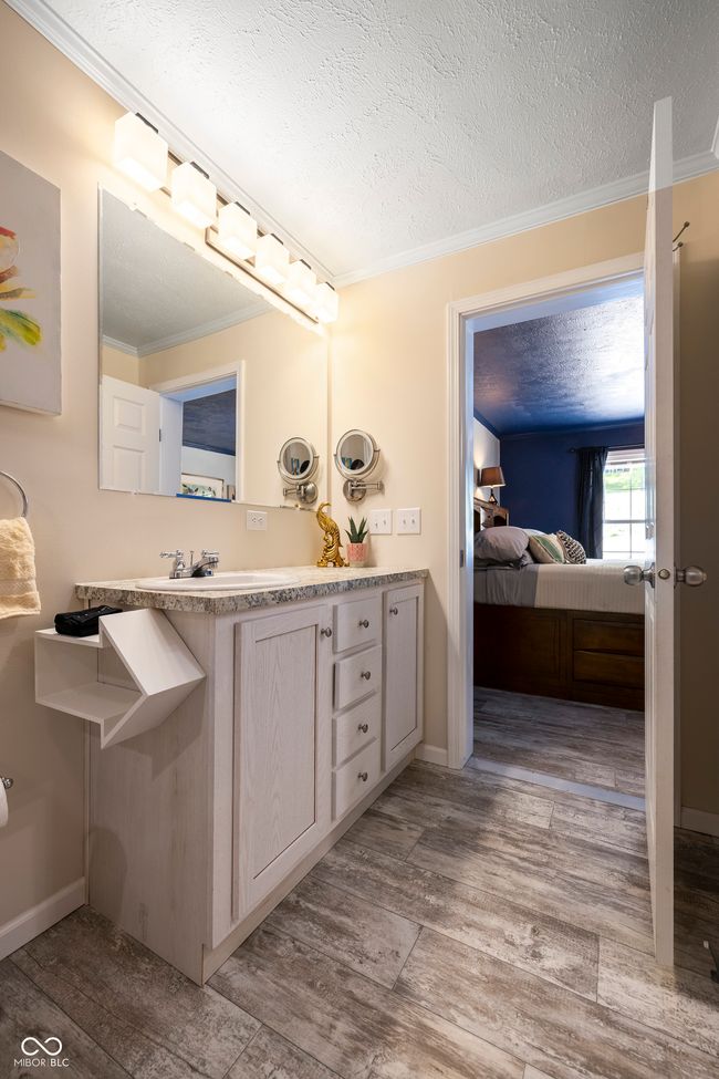 bathroom with crown molding, connected bathroom, vanity, a textured ceiling, and wood finished floors | Image 27