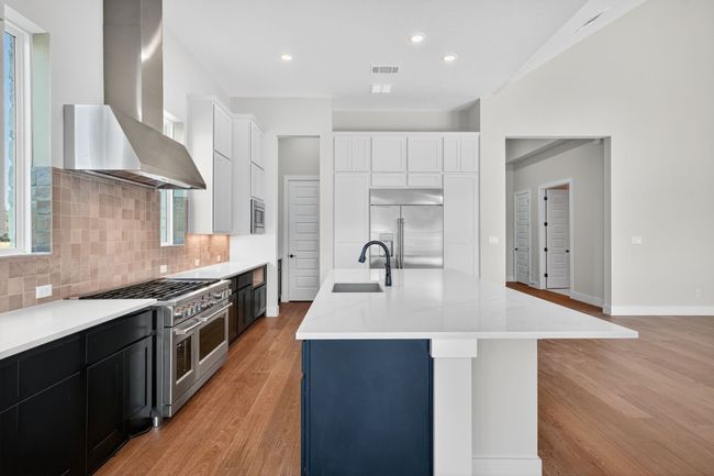 Kitchen with light wood-type flooring, wall chimney exhaust hood, built in appliances, light stone counters, and recessed lighting | Image 8