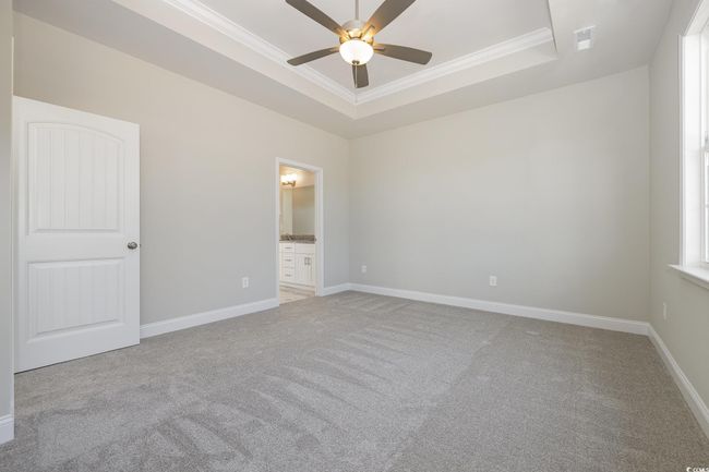 Unfurnished bedroom featuring ensuite bathroom, ornamental molding, light colored carpet, a raised ceiling, and ceiling fan | Image 16