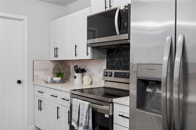 Kitchen with stainless steel appliances, light countertops, white cabinetry, and decorative backsplash | Image 12