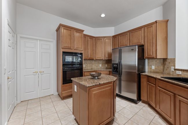 Kitchen with a kitchen island, backsplash, light tile patterned floors, black appliances, and light stone countertops | Image 15