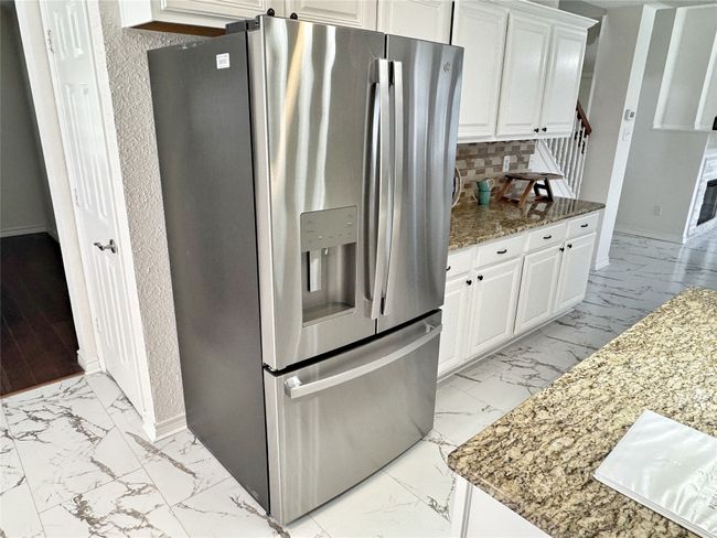 Kitchen featuring stainless steel fridge, light marble finish flooring, light stone counters, white cabinets, and backsplash | Image 13