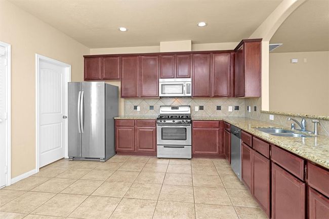 The spacious kitchen offers 42" upper cabinets, granite countertops, and a stylish tile backsplash with granite inlays. Equipped with stainless steel appliances—including a gas range and built-in microwave—the kitchen combines functionality and elegance. | Image 9