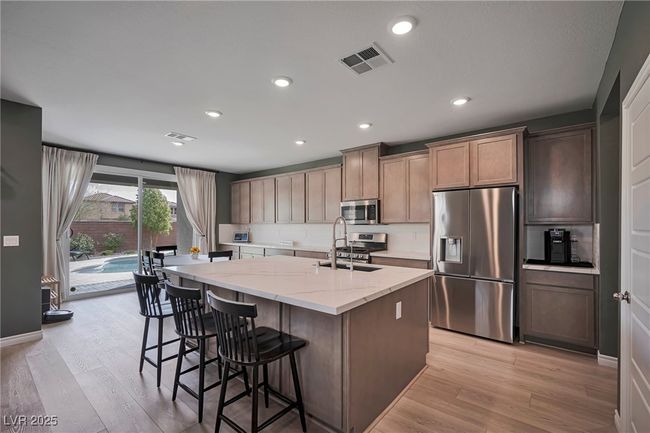 Kitchen featuring light stone counters, a sink, light wood finished floors, appliances with stainless steel finishes, and visible vents | Image 7