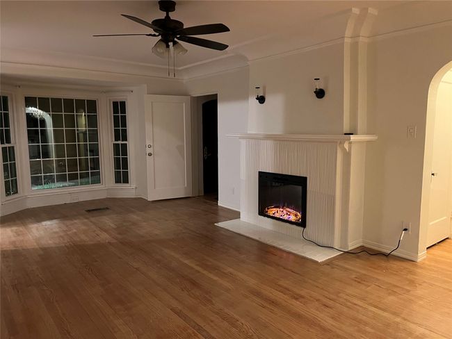 Unfurnished living room with wood finished floors, a ceiling fan, a fireplace with flush hearth, arched walkways, and baseboards | Image 8