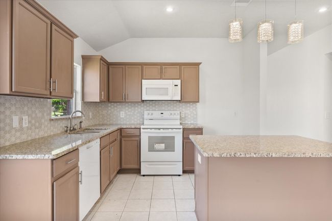 Kitchen featuring white appliances, a sink, lofted ceiling, backsplash, and pendant lighting | Image 8