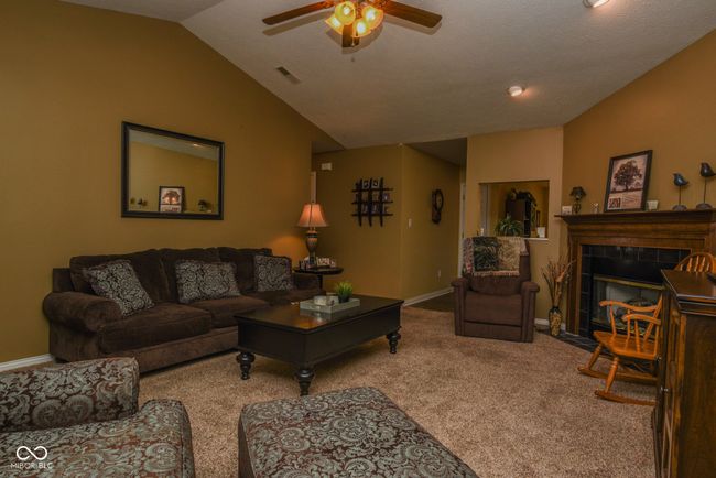 living area with lofted ceiling, carpet, a ceiling fan, baseboards, and a tile fireplace | Image 4