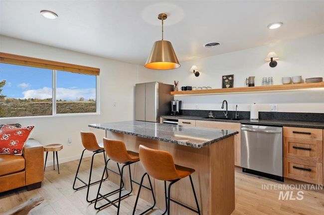 Kitchen with stainless steel dishwasher, a breakfast bar, a kitchen island, open shelves, and light wood-style floors | Image 35
