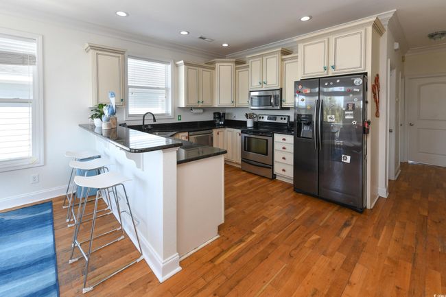 Kitchen featuring stainless steel appliances, ornamental molding, a sink, a peninsula, and a kitchen breakfast bar | Image 4