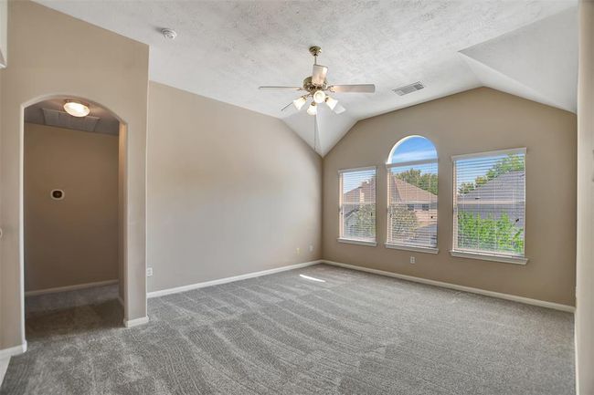 Spacious, carpeted room with vaulted ceiling and ceiling fan. Features large arched windows offering plenty of natural light and a view of the neighborhood. Neutral walls create a bright and airy ambiance. | Image 28