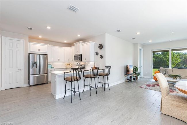 Kitchen featuring a breakfast bar, stainless steel appliances, visible vents, open floor plan, and white cabinetry | Image 9