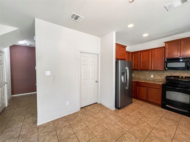 Kitchen with black appliances, backsplash, recessed lighting, light tile patterned floors, and brown cabinets | Image 9