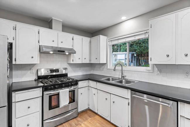 Kitchen with stainless steel appliances, under cabinet range hood, a sink, and dark countertops | Image 11