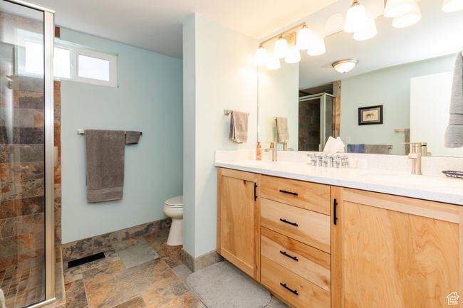 Full bath featuring a sink, a stall shower, double vanity, toilet, and stone finish floor | Image 28